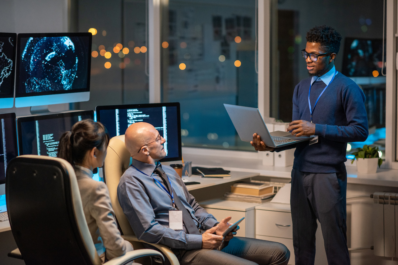 Threat Alliance | Fortifying Your Defense: Exploring the Elements of Layered Security Businessman with laptop talking with team looking at elements of layered security